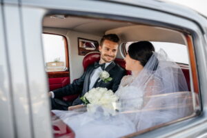 A young couple, just married, in the backseat of a classic car